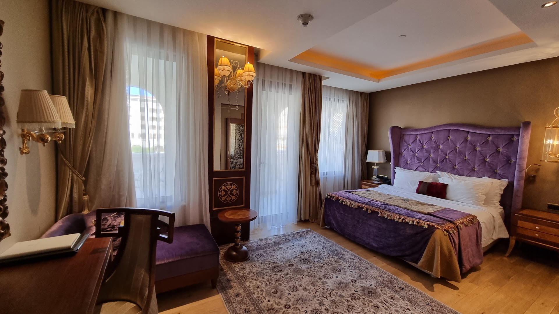 Titanic Mardan Palace numurs ar violetu samta gultas galvgali, mīkstu paklāju un gaišiem aizkariem Antaljas piekrastē