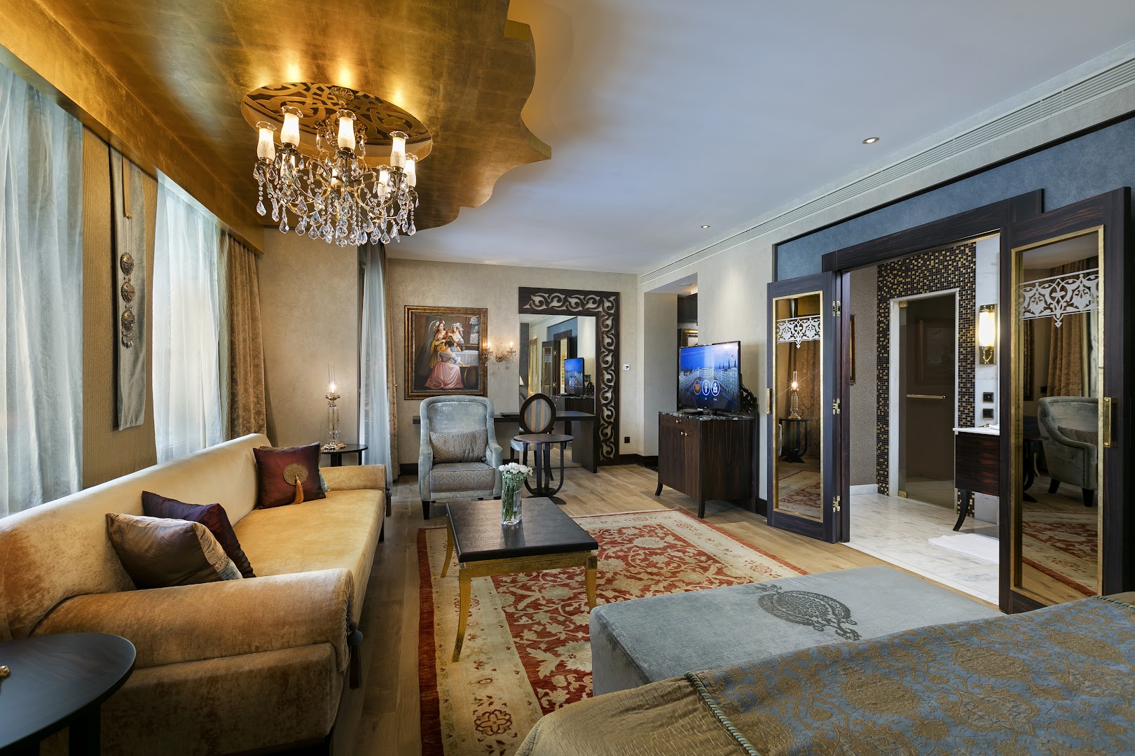 Titanic Mardan Palace viesistabas zona ar zeltītu lustru, ērtu dīvānu un klasiskām gleznām Antaljas reģionā