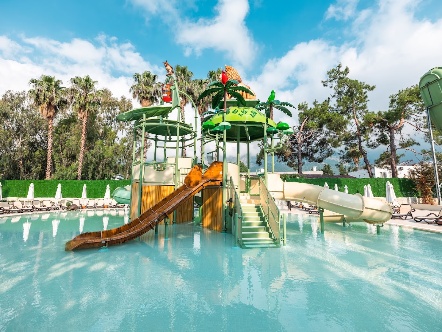 Greenwood Kemer Resort āra baseina zona bērniem ar dekoratīvām figūrām, slidkalniņiem un saulessargiem fonā