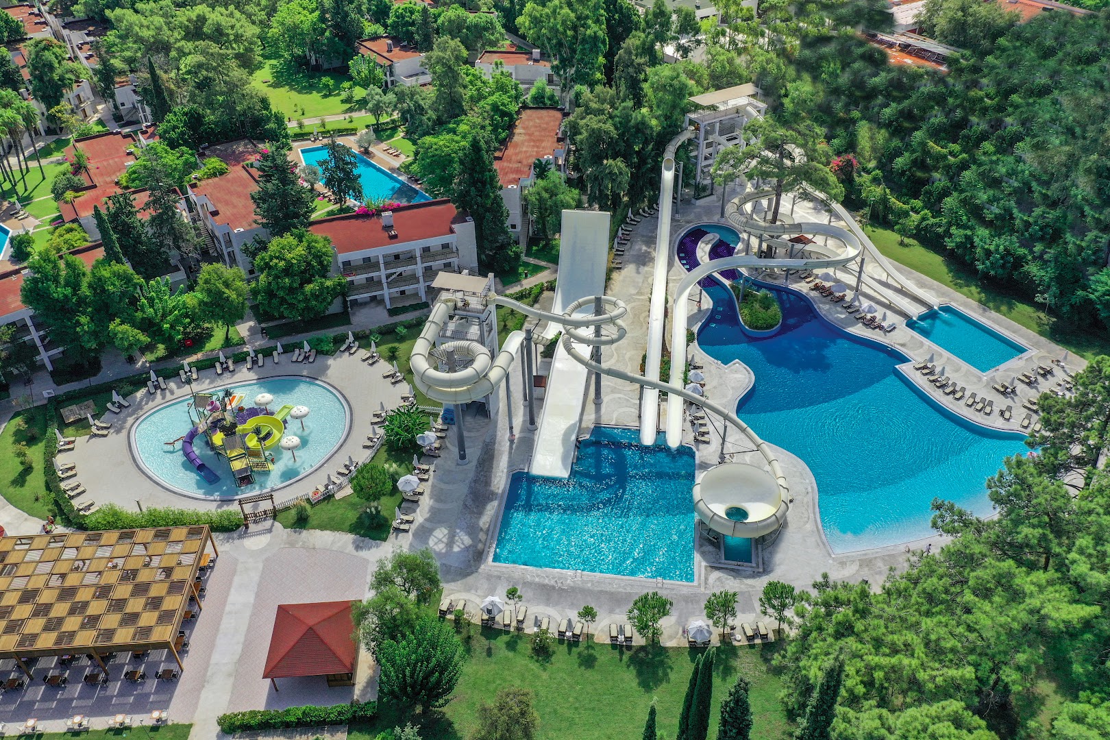 Sherwood Exclusive Kemer teritorijas skats no augšas — baseini, ūdens atrakcijas un viesnīcas korpusi zaļojošu koku un dārzu ielenkumā