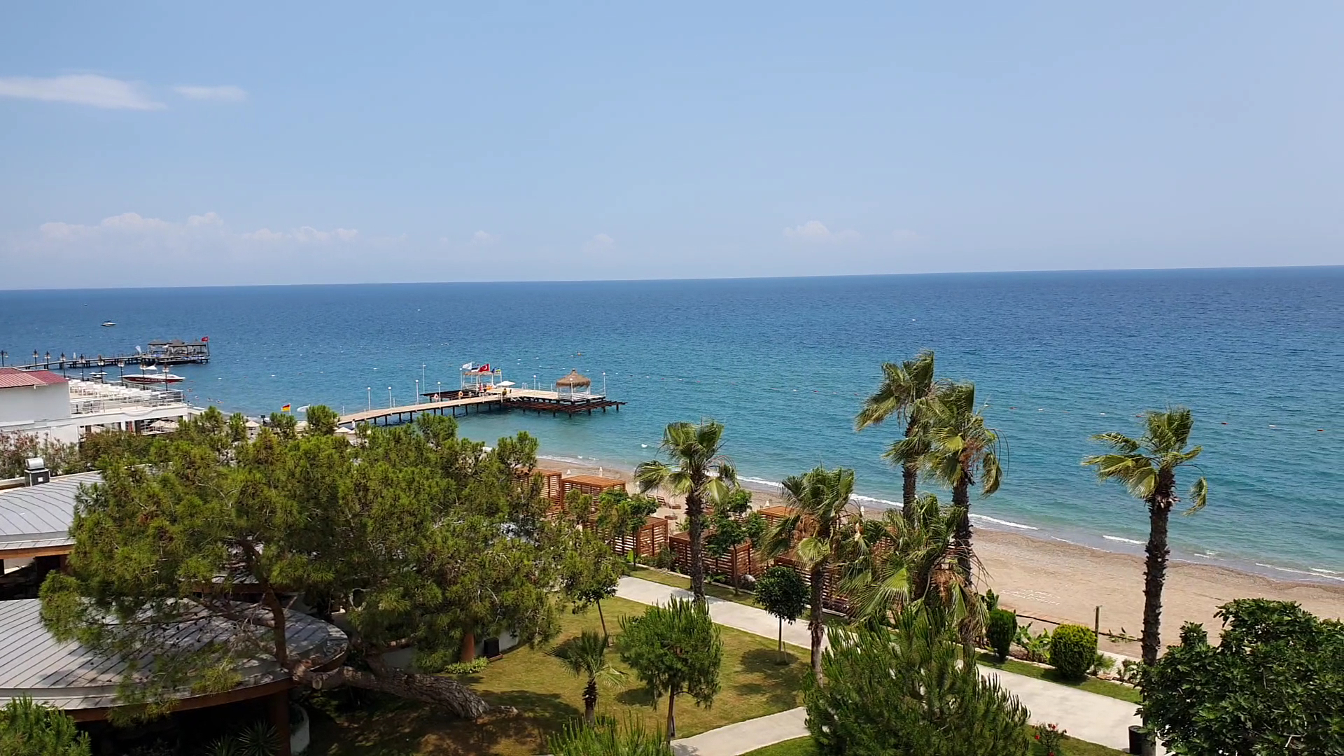 Sherwood Exclusive Kemer skats no augšas uz Vidusjūras piekrasti, koka piestātni un smilšu pludmali, ko ieskauj zaļas priedes un palmas.