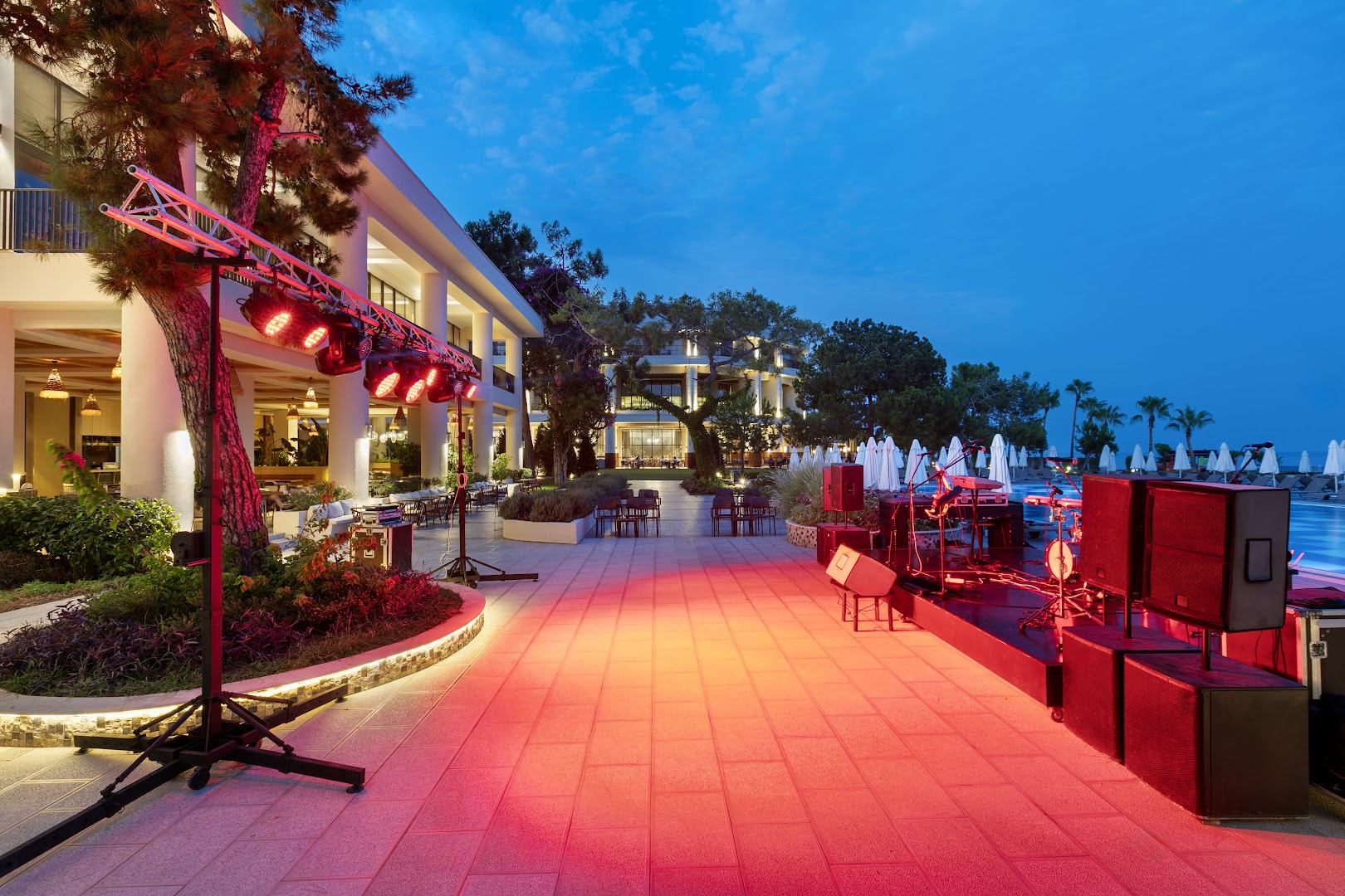 Sherwood Exclusive Kemer vakara izklaides zona ar skatuvi, mūzikas instrumentiem un sarkanu apgaismojumu pie viesnīcas galvenās ēkas un baseina