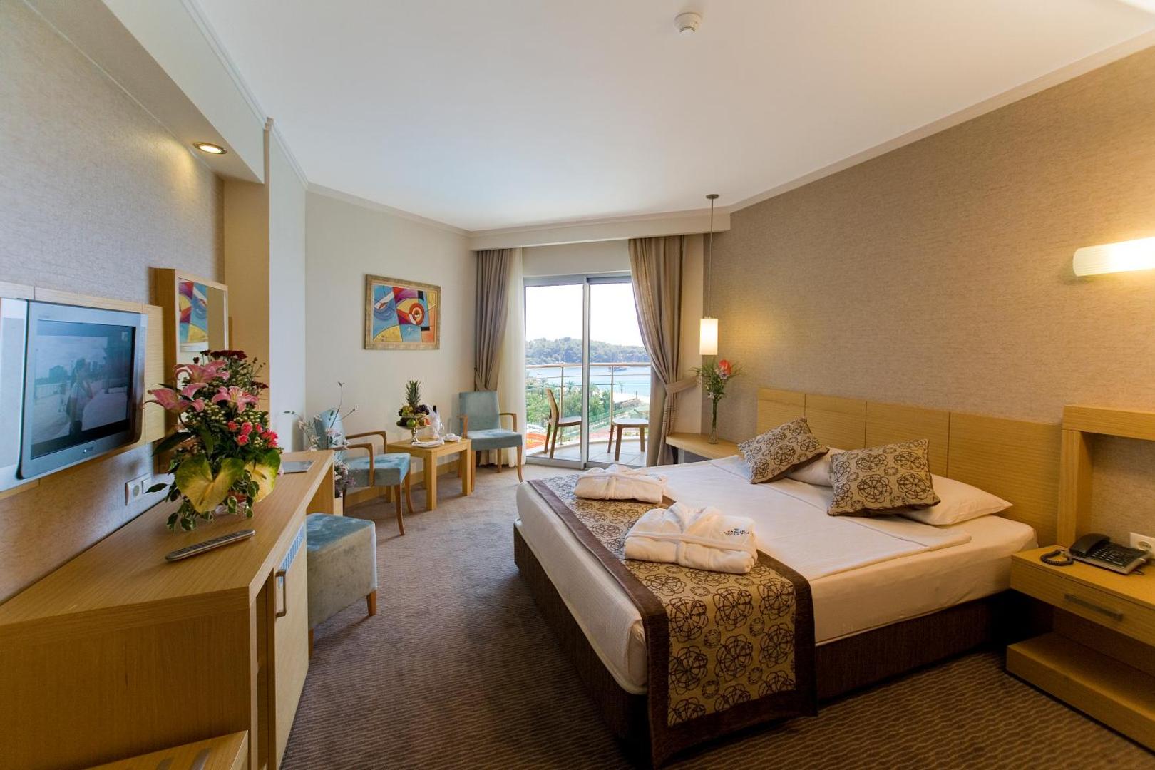 Saphir Resort & Spa gaišs viesnīcas numurs ar divguļamo gultu, atpūtas zonu un balkonu ar skatu uz jūru