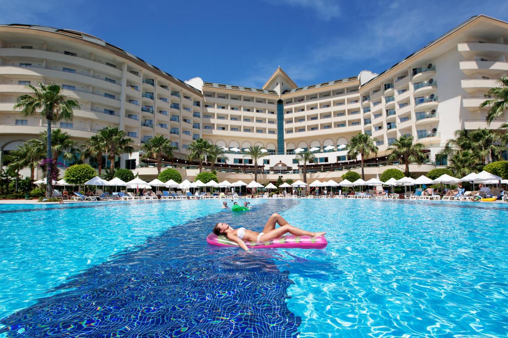 Saphir Resort & Spa lielais āra baseins un viesnīcas galvenā ēka ar saulessargiem un atpūtas krēsliem saulainā dienā