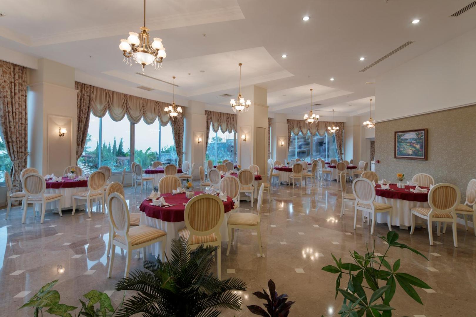 Saphir Resort & Spa klasiskā stila restorāns ar apaļiem galdiem, sarkanu galdautu un lieliem logiem Alānijā, Turcijā