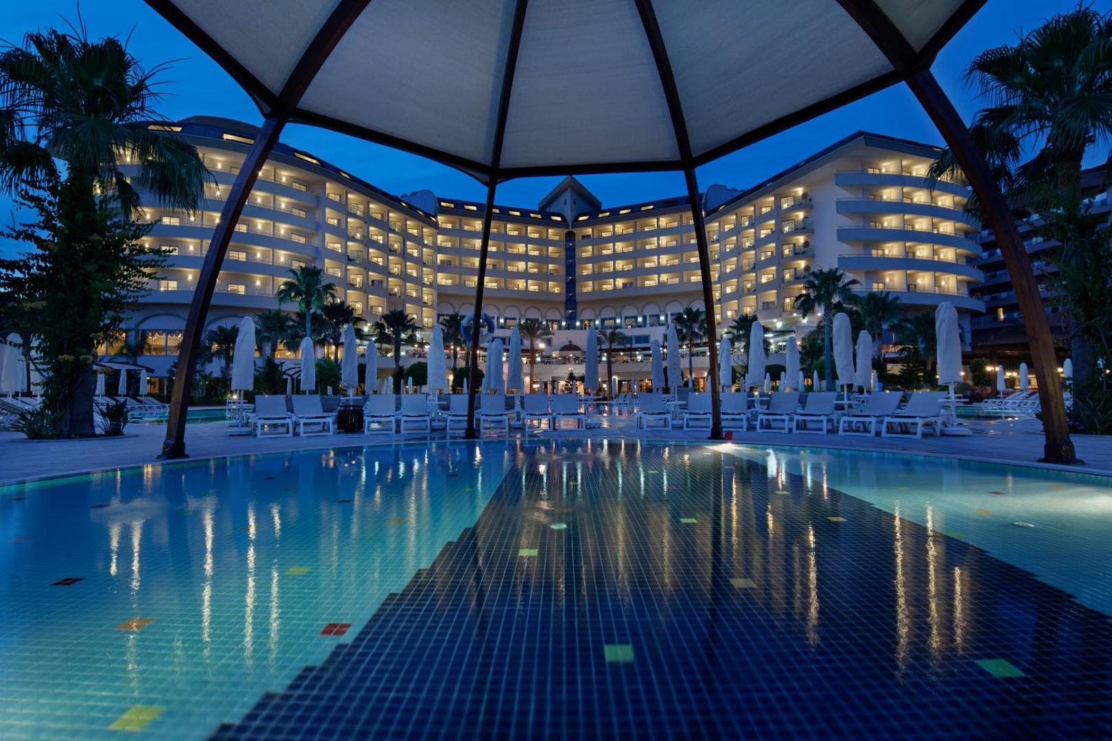 Saphir Resort & Spa viesnīcas galvenā ēka naktī ar izgaismotiem balkoniem un baseinu priekšplānā — skats no atpūtas zonas