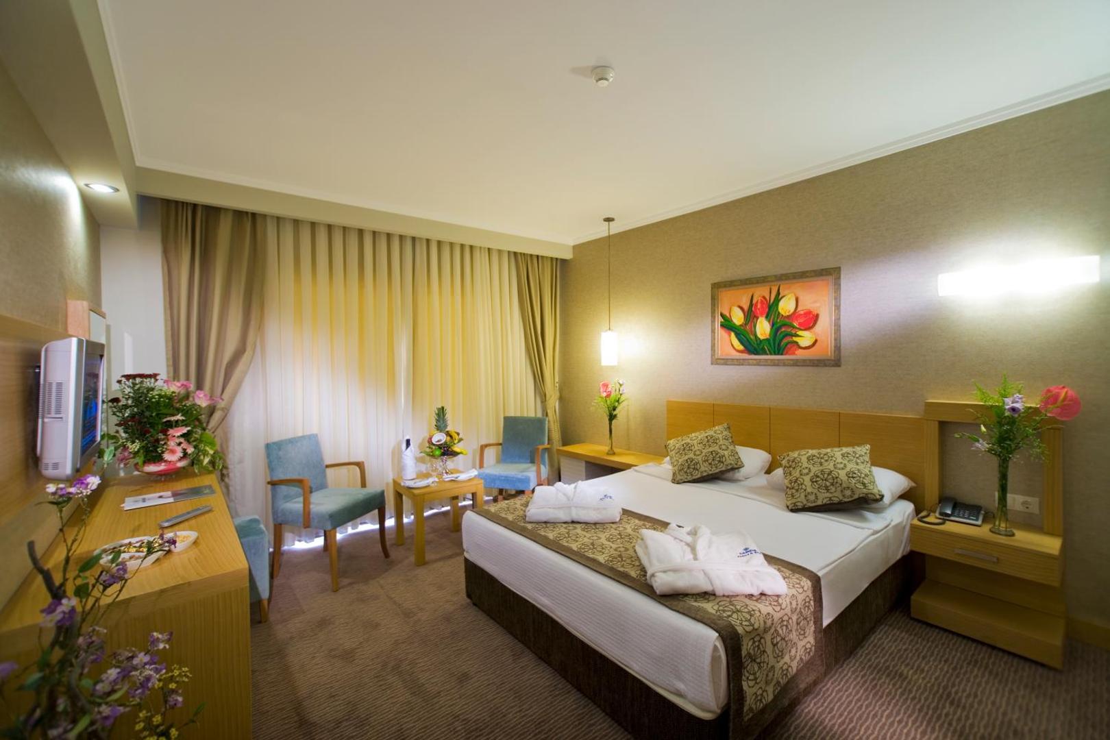 Saphir Resort & Spa mājīgs divvietīgs numurs ar gaišām mēbelēm, atpūtas zonu un ziedu dekorācijām siltos toņos