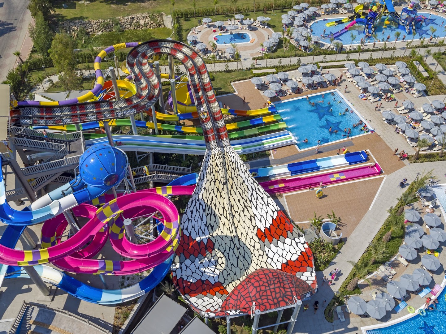 Royal Seginus viesnīcas akvaparka slidkalniņi un bērnu baseini Antaljā — tuvplāns uz kobras formas atrakciju un saulessargiem pie baseina