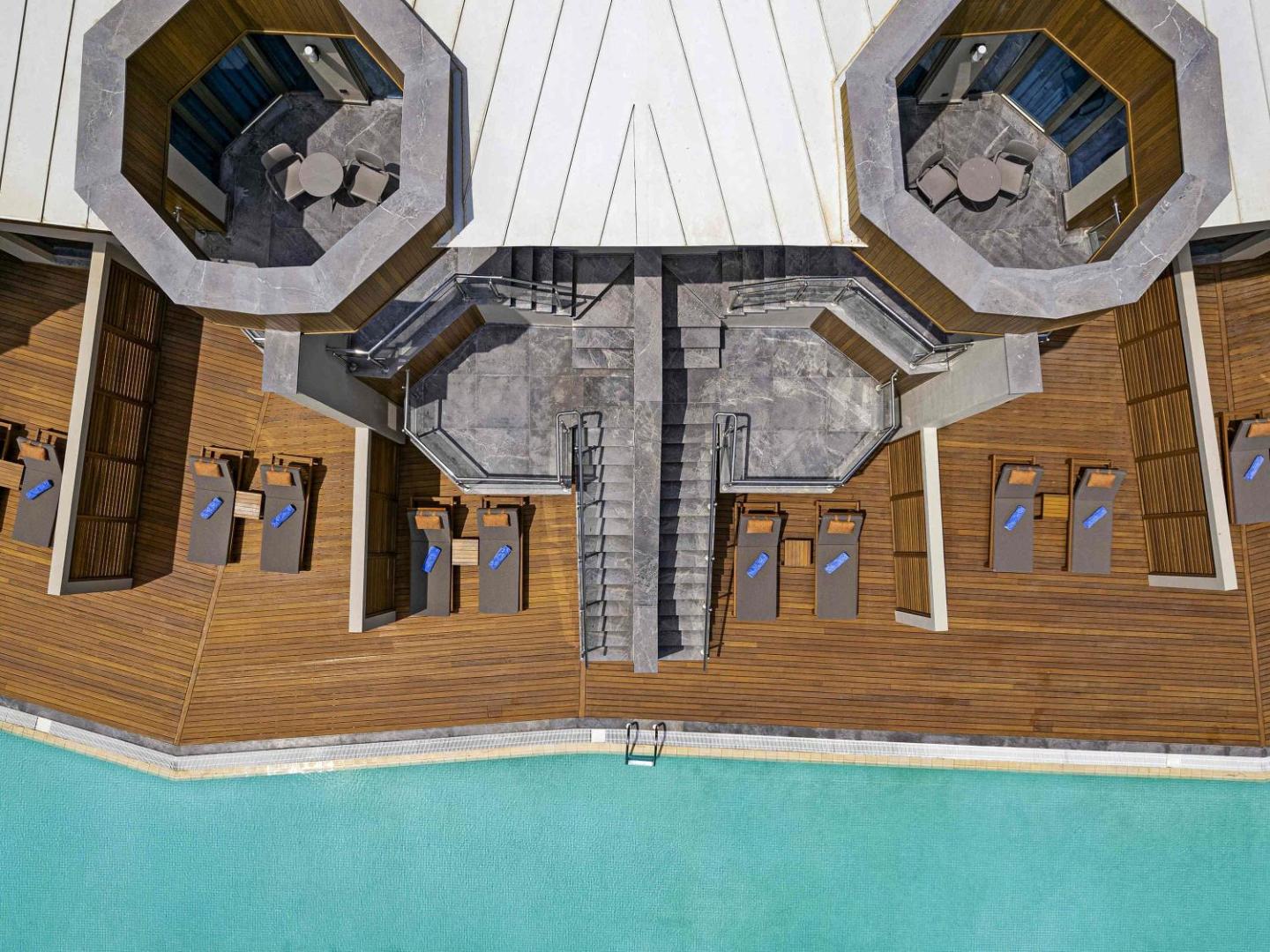 Rixos Sungate numuru terases ar koka klāju un sauļošanās krēsliem pie baseina, skats no augšas uz modernu arhitektūru