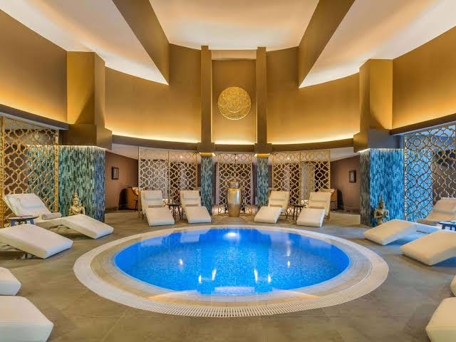 Rixos Sungate spa centra iekštelpu baseins ar atpūtas krēsliem — grezns interjers ar zelta akcentiem un mierīgu apgaismojumu