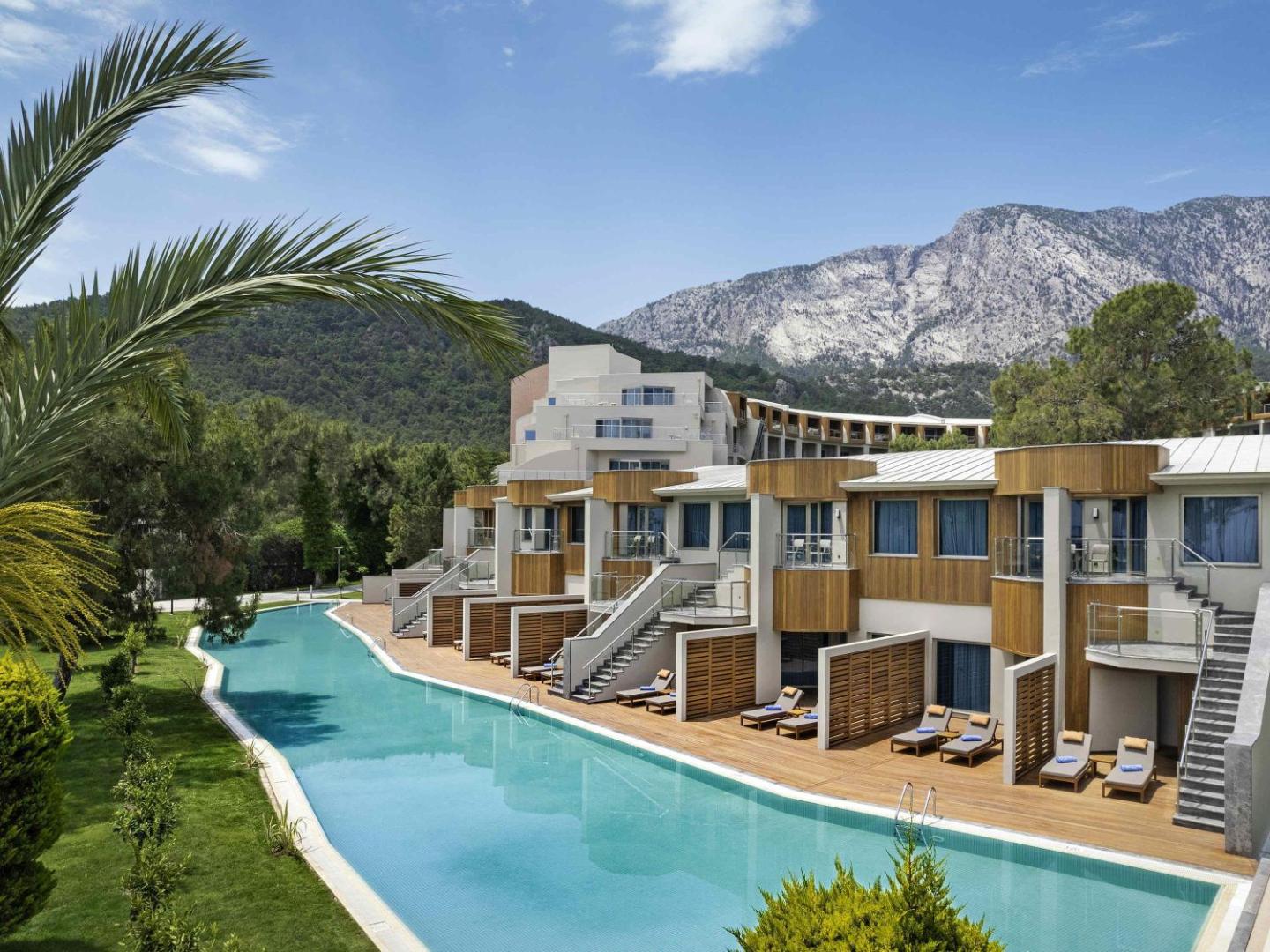 Rixos Sungate moderni numuri ar tiešu piekļuvi baseinam un koka terasēm uz kalnu un priežu meža fona