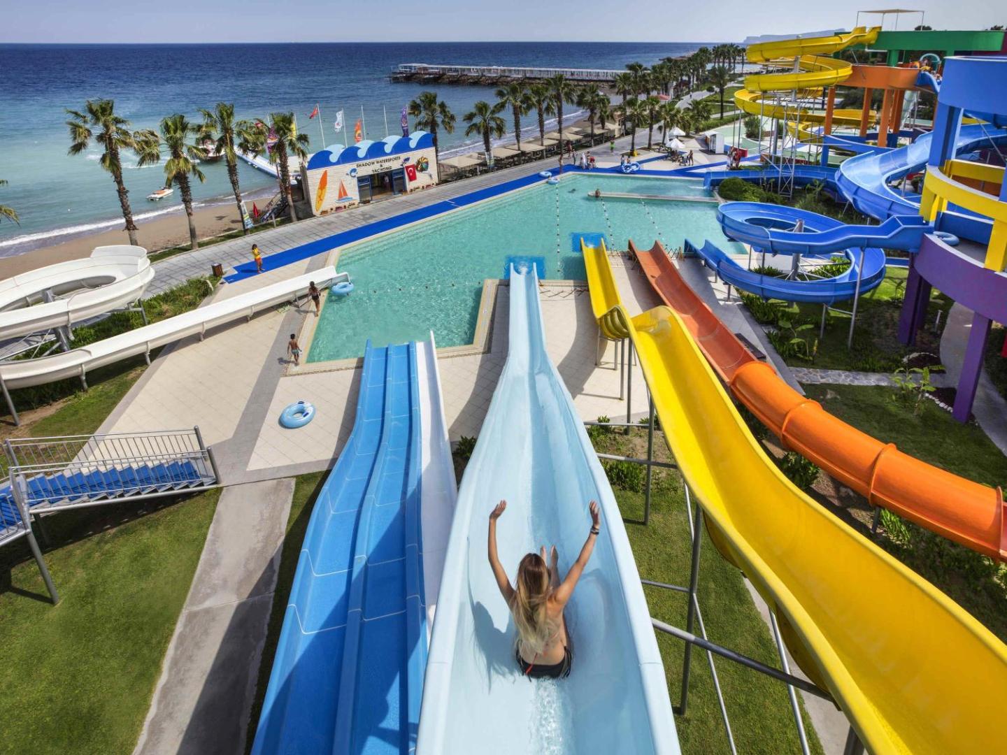 Rixos Sungate akvaparks ar krāsainiem ūdens slidkalniņiem un skatu uz Vidusjūras piekrasti un palmu aleju.