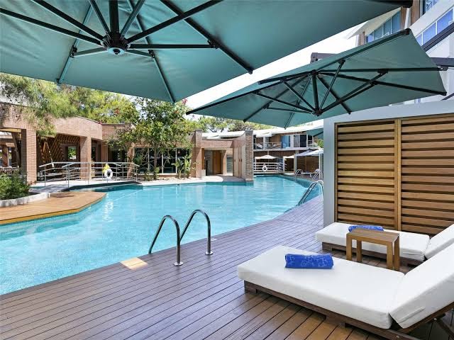 Rixos Sungate atpūtas zona ar koka terasi, mīkstiem sauļošanās krēsliem un lieliem saulessargiem pie baseina.
