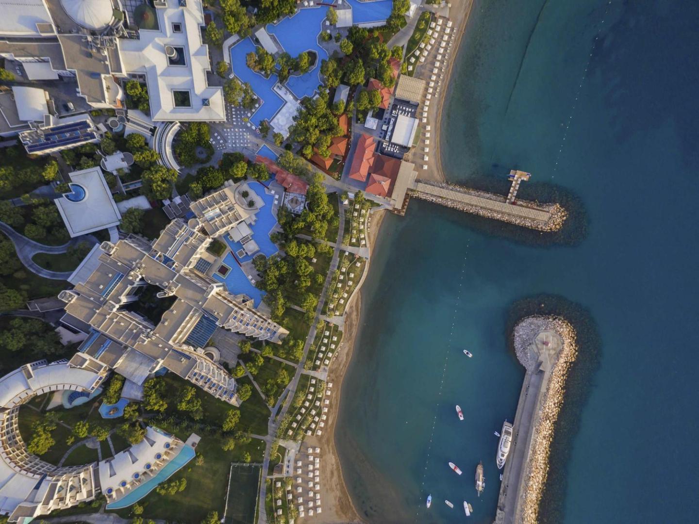 Rixos Sungate viesnīcas teritorijas skats no augšas uz baseiniem, pludmali un piestātnēm dzidri zilā jūras līča krastā
