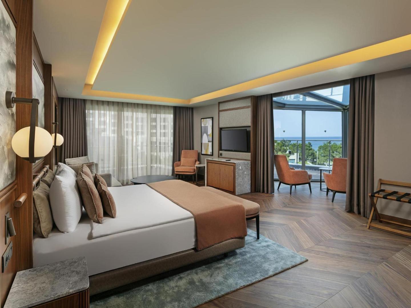 Rixos Sungate gaišs numurs ar panorāmas logiem, skatu uz jūru un priedēm — moderna guļamistaba ar atpūtas zonu