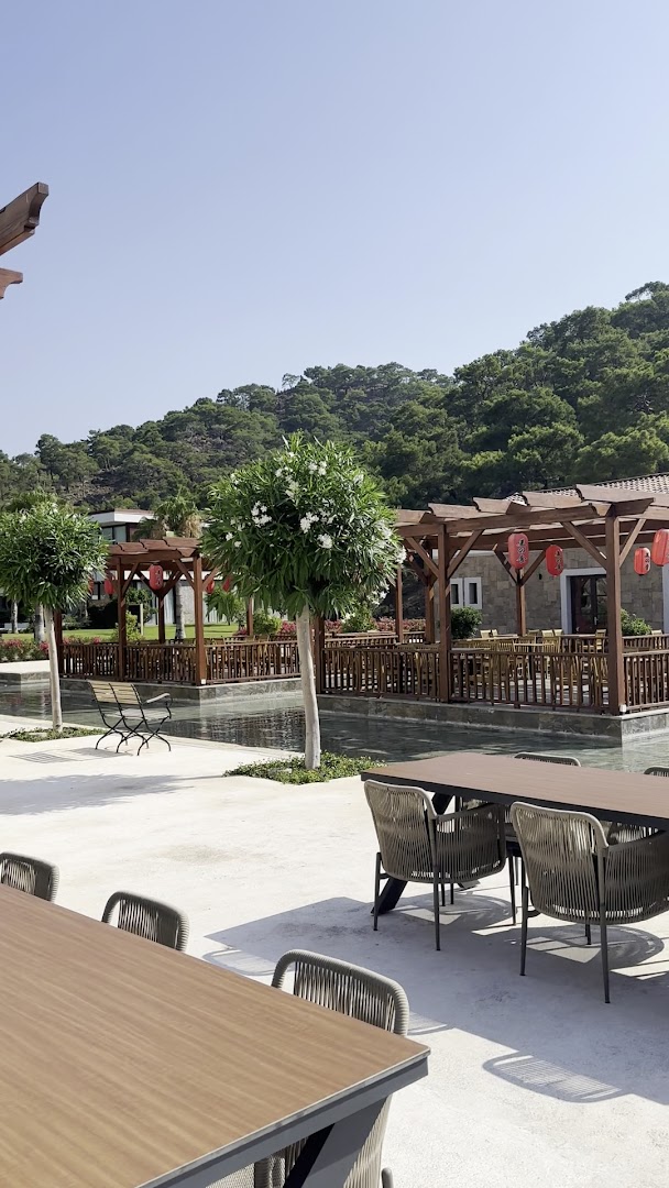 Rixos Premium Tekirova āra terase ar koka lapenēm pie ūdens kanāla un skatu uz priežu mežu klātiem kalniem