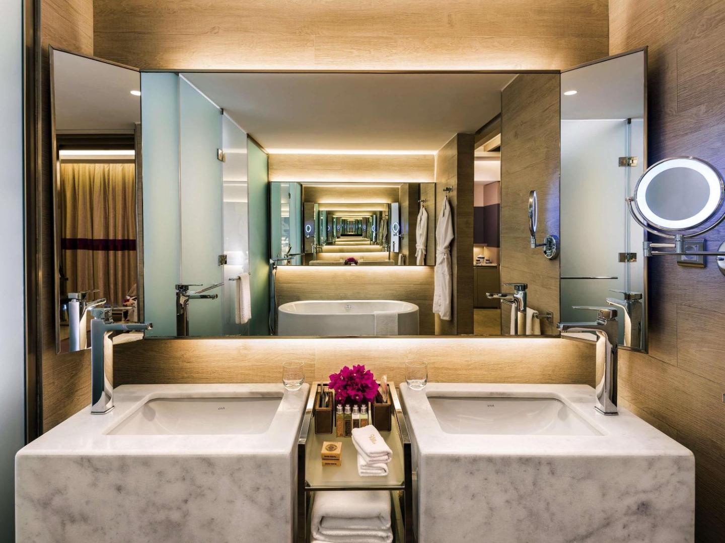 Rixos Premium Tekirova numura vannas istaba ar divām marmora izlietnēm, lielu spoguli un vannu fonā