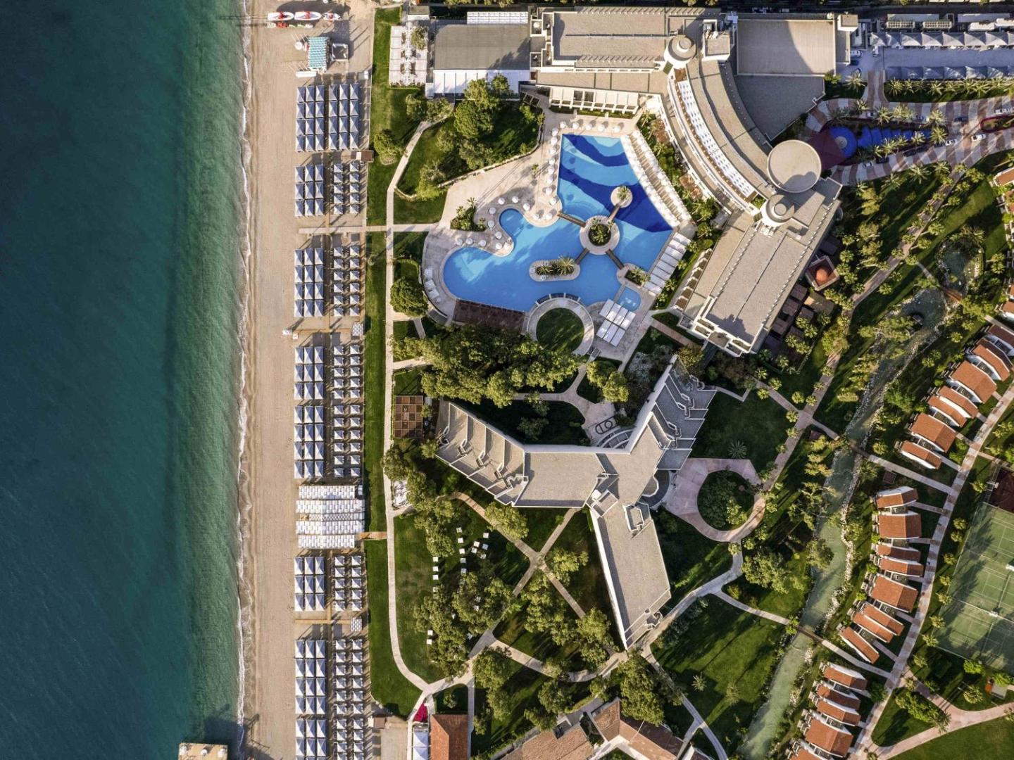 Rixos Premium Tekirova teritorijas skats no putna lidojuma — baseini, dārzi, pludmales zona un numuru korpusi