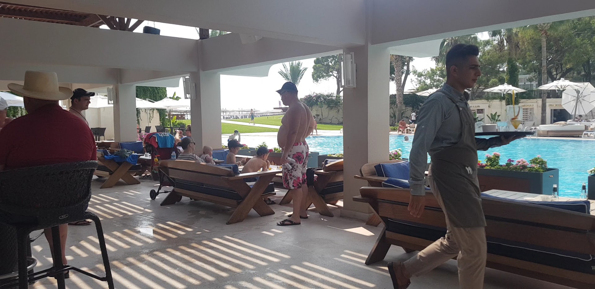 Rixos Premium Tekirova bārs pie baseina ar atpūtas zonu zem nojumes un skatu uz zilo baseinu un palmām