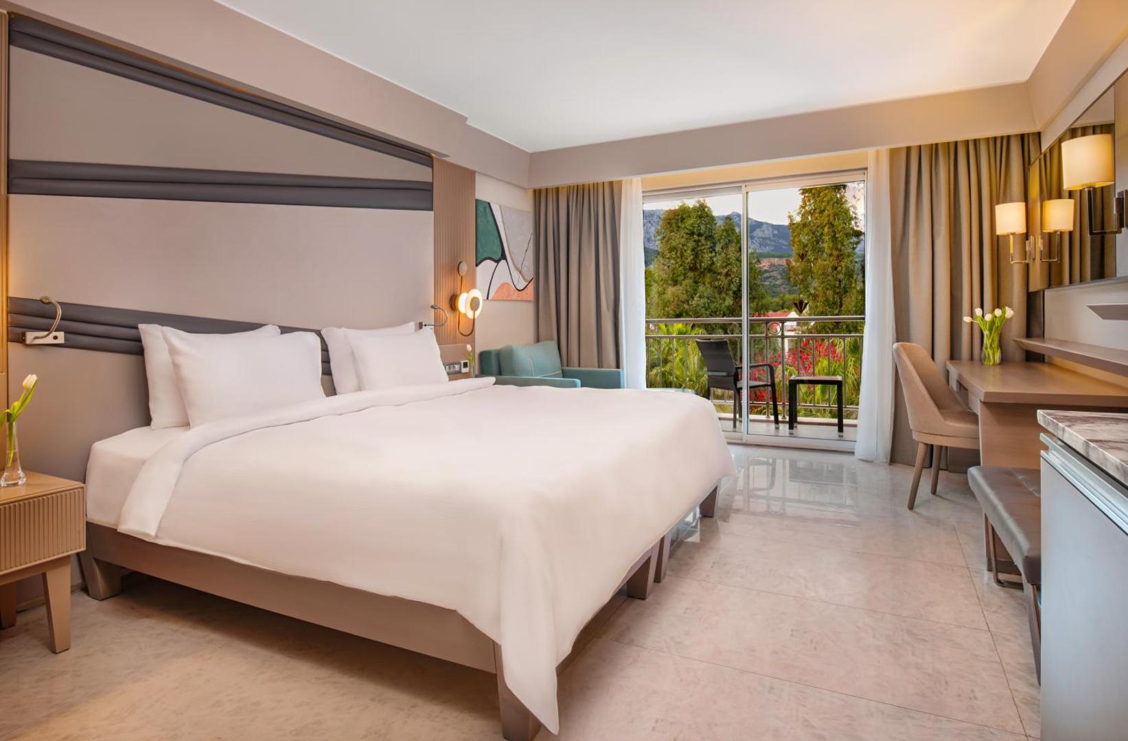 Rixos Premium Tekirova mājīgs numurs ar balkonu, rakstāmgaldu un skatu uz viesnīcas dārzu un apkārtnes kalniem