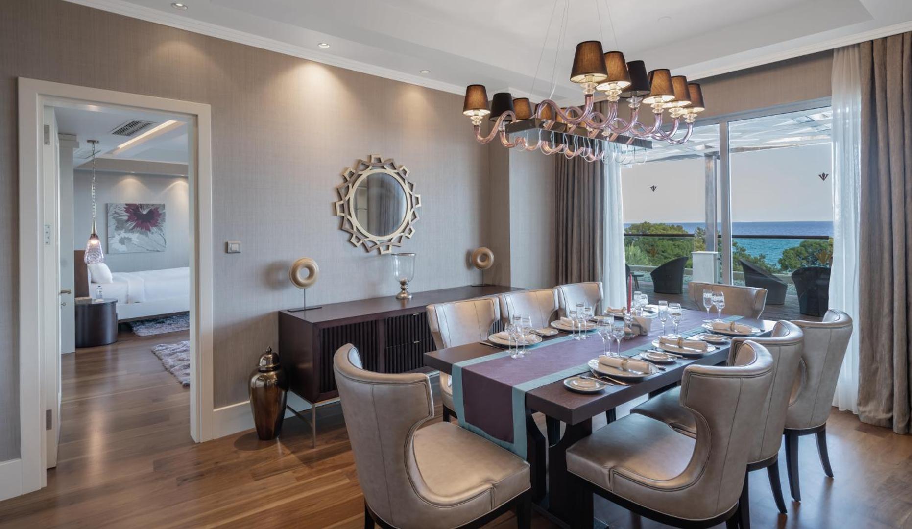 Rixos Premium Tekirova eleganta ēdamzāle ar lielu galdu, dizaina lampu un skatu uz jūru no terases