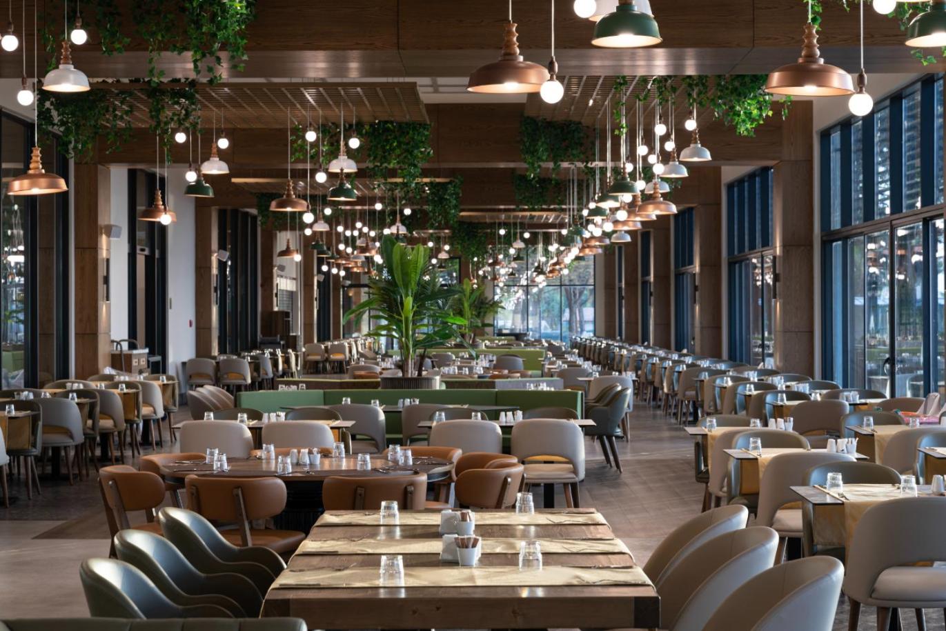 Moderns Swandor Hotels & Resorts galvenais restorāns ar stilīgu apgaismojumu, koka elementiem un plašu sēdvietu zonu