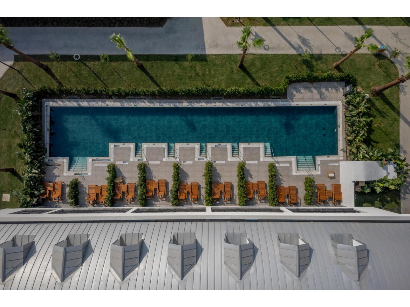 Swandor Hotels & Resorts baseins no putna lidojuma — koka sauļošanās krēsli, zaļš mauriņš un moderna arhitektūra