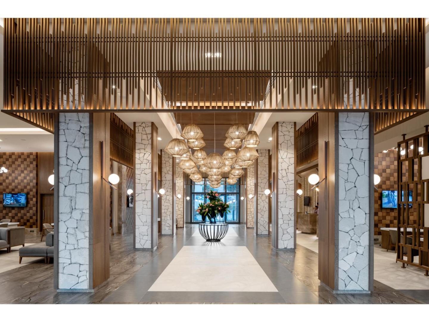 Swandor Hotels & Resorts modernais vestibils ar akmens kolonnām, dizaina gaismekļiem un koka apdari — plaša un gaiša viesnīcas lobby zona