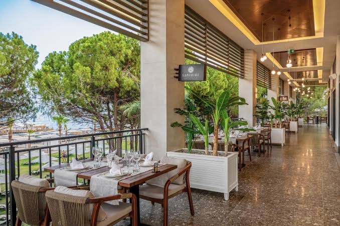 Swandor Hotels & Resorts restorāna āra terase ar klātiem galdiem, skatu uz priedēm un jūras piekrasti Kemeras reģionā