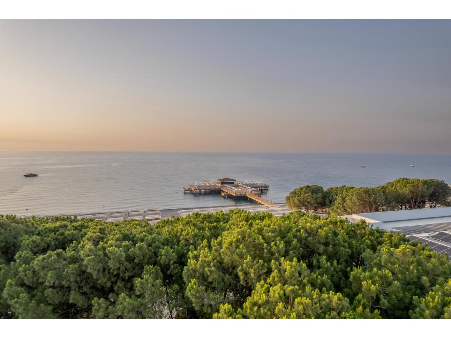 Skats no augšas uz Swandor Hotels & Resorts koka piestātni un pludmali saulrieta laikā Vidusjūras piekrastē