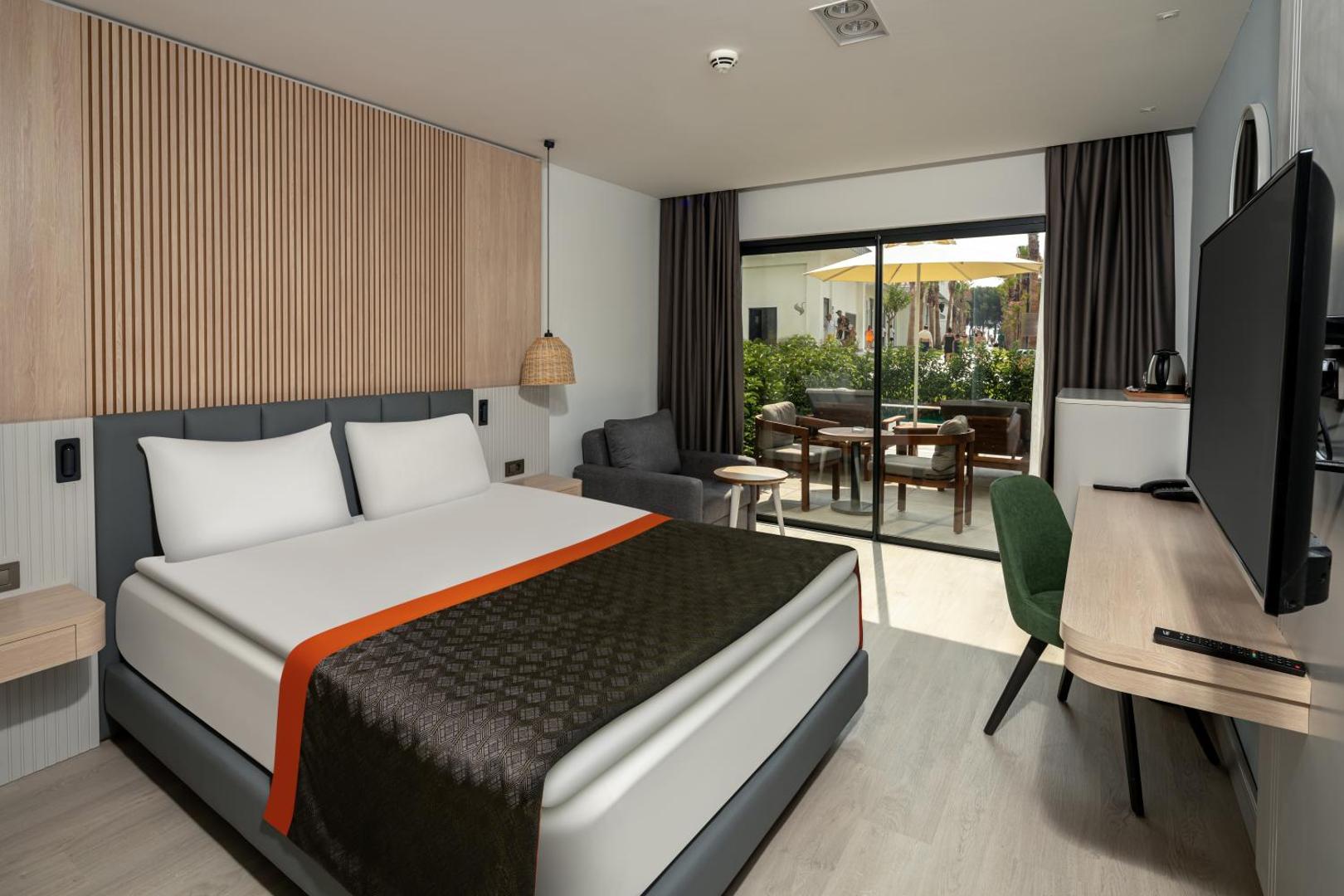 Swandor Hotels & Resorts numura interjers ar koka apdari, lielu gultu un mēbelētu terasi saulainā pēcpusdienā