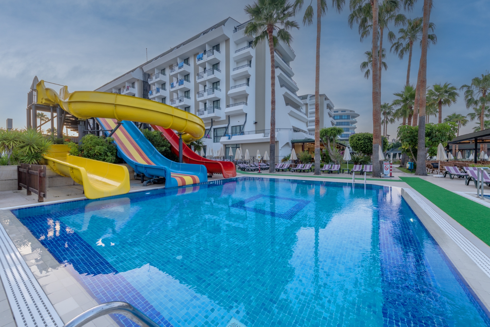 Meryan Hotel bērnu baseins ar krāsainiem ūdens slidkalniņiem un viesnīcas ēku fonā — piemērots ģimenes atpūtai ar bērniem.