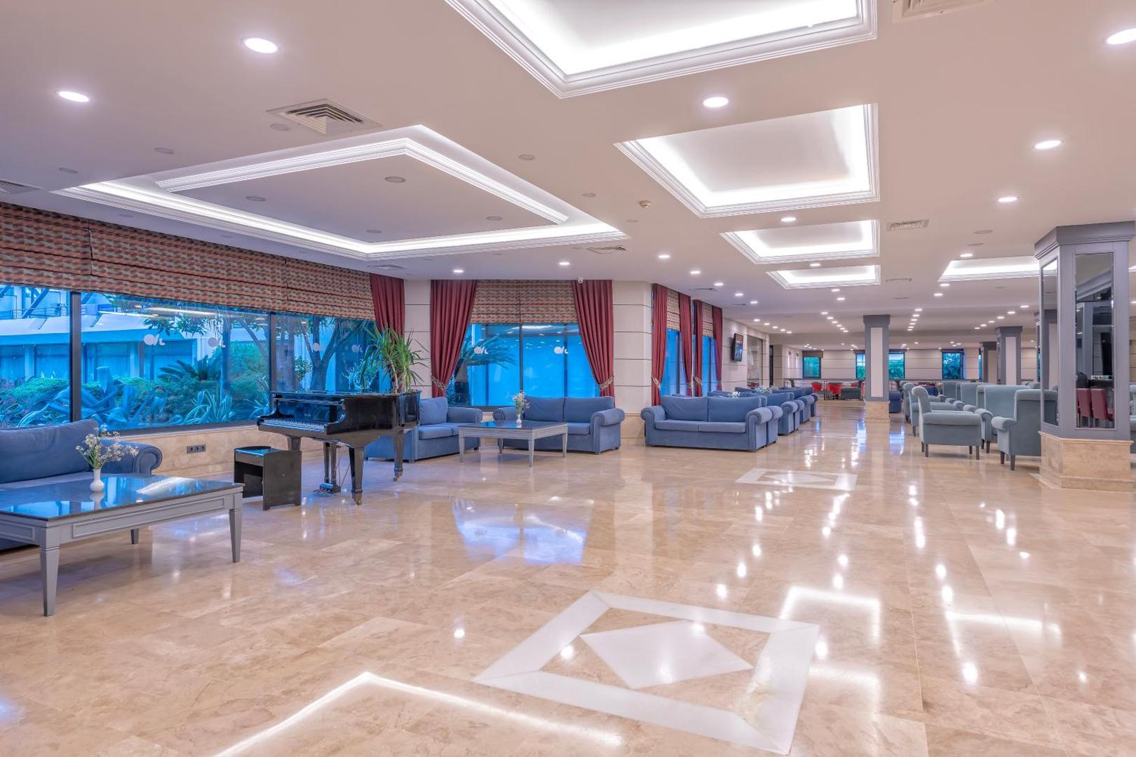 Meryan Hotel lobby bāra zona ar ziliem dīvāniem, klavierēm un lieliem logiem uz dārzu