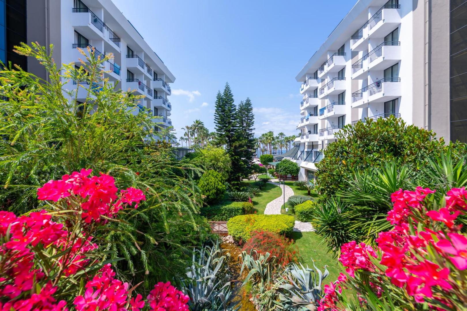 Meryan Hotel iekšpagalms ar ziedošiem krūmiem, koptu zālienu un gājēju celiņiem starp viesnīcas korpusiem