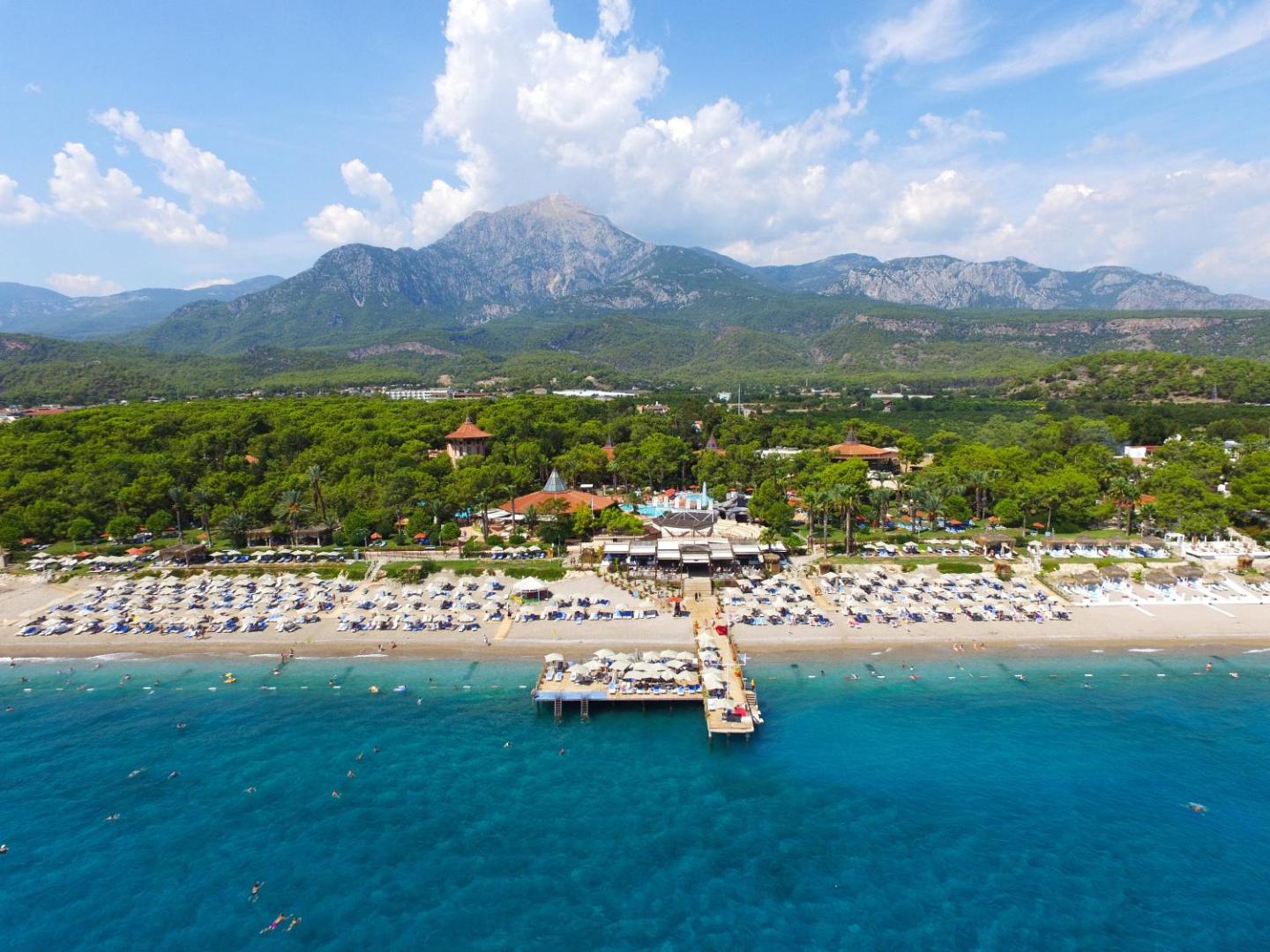 Marti Myra Hotel panorāmas skats uz piekrasti un kalniem Tekirovā — plaša pludmale ar piestātni un priežu meža ieskauta teritorija