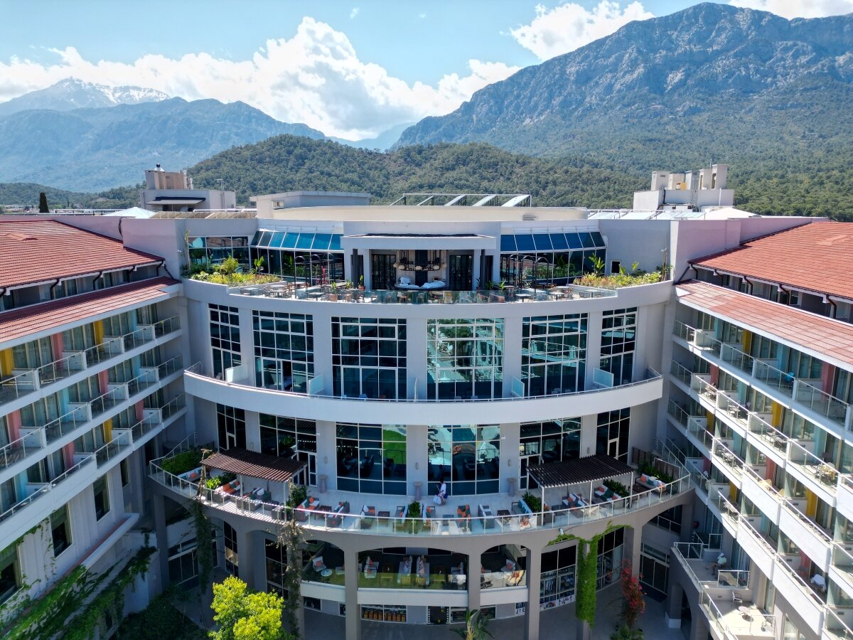 Akra Kemer viesnīcas modernā arhitektūra ar stiklotiem balkoniem un terasēm uz kalnu fona Kemeras piekrastē