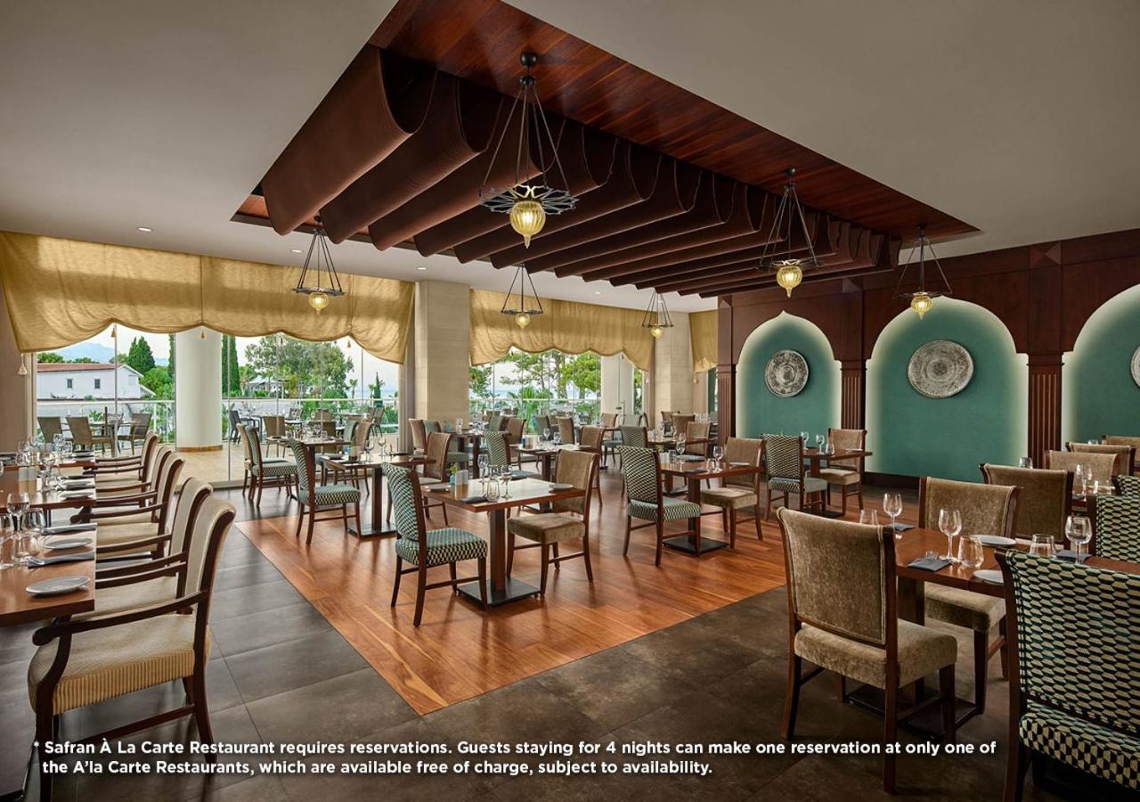 Akra Kemer viesnīcas Safran à la carte restorāns ar elegantiem galdiem, koka detaļām un skatu uz dārzu Kemeras reģionā