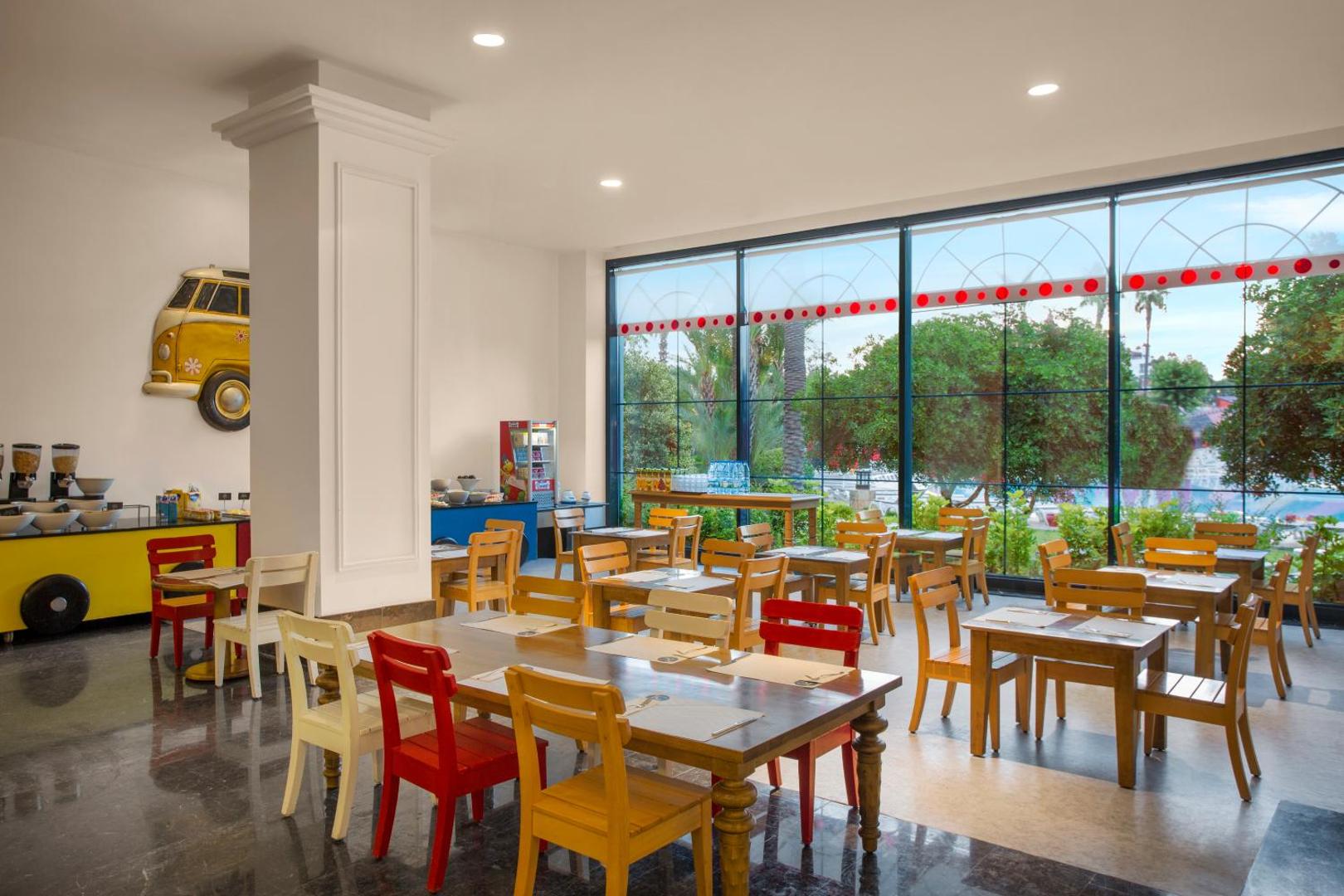 IC Hotels Santai Family Resort bērnu restorāna zona ar krāsainiem krēsliem, rotaļīgu dizainu un skatu uz dārzu