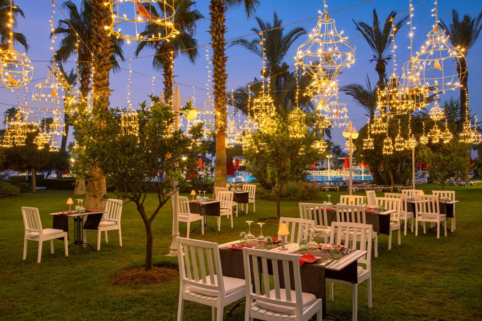 IC Hotels Santai Family Resort āra restorāns dārzā ar dekoratīvām gaismas virtenēm un baltiem krēsliem vakarā