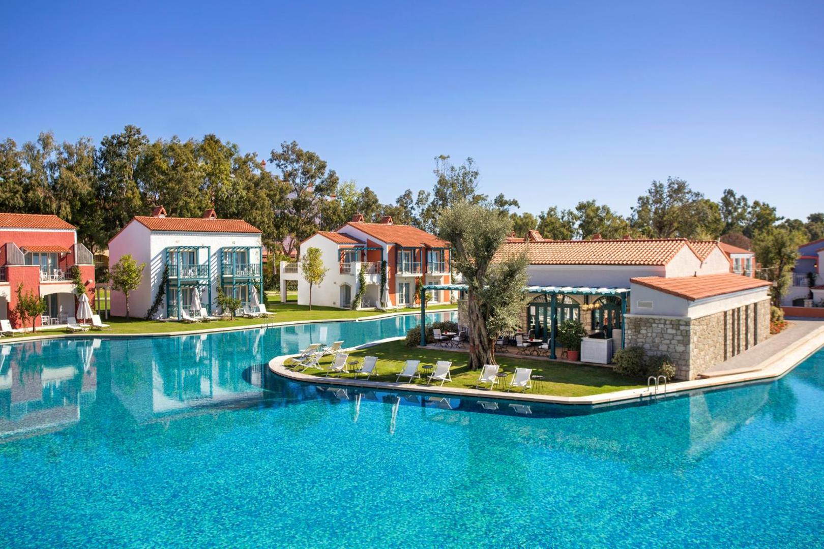 IC Hotels Santai Family Resort āra baseins ar ziliem flīžu klājumiem un apkārt esošajām bungalo tipa mājiņām Belekā, Turcijā