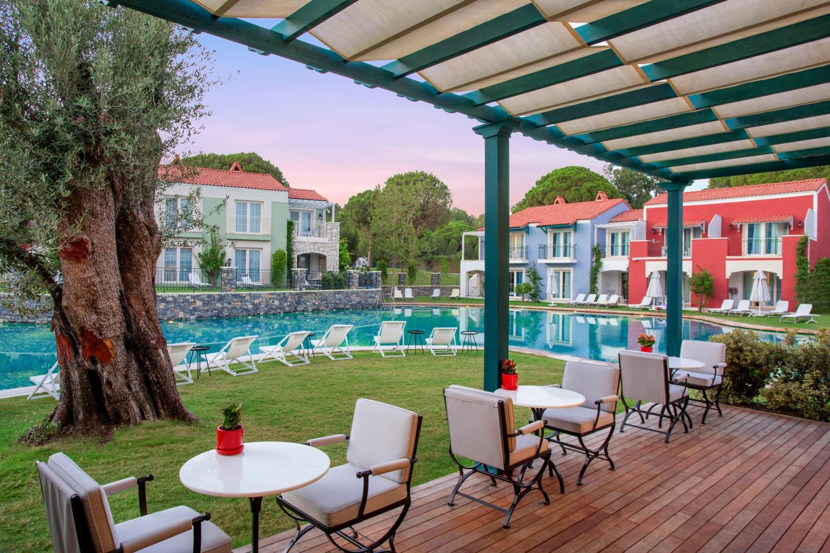 IC Hotels Santai Family Resort āra terase ar galdiņiem zem nojumes, skatu uz dārzu, baseinu un krāsainiem numuru korpusiem