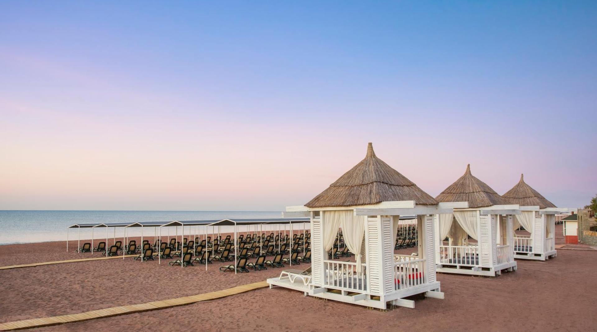 IC Hotels Santai Family Resort privātās pludmales bungalo ar niedru jumtiem un baltiem aizkariem Belekas piekrastē saulrieta gaismā