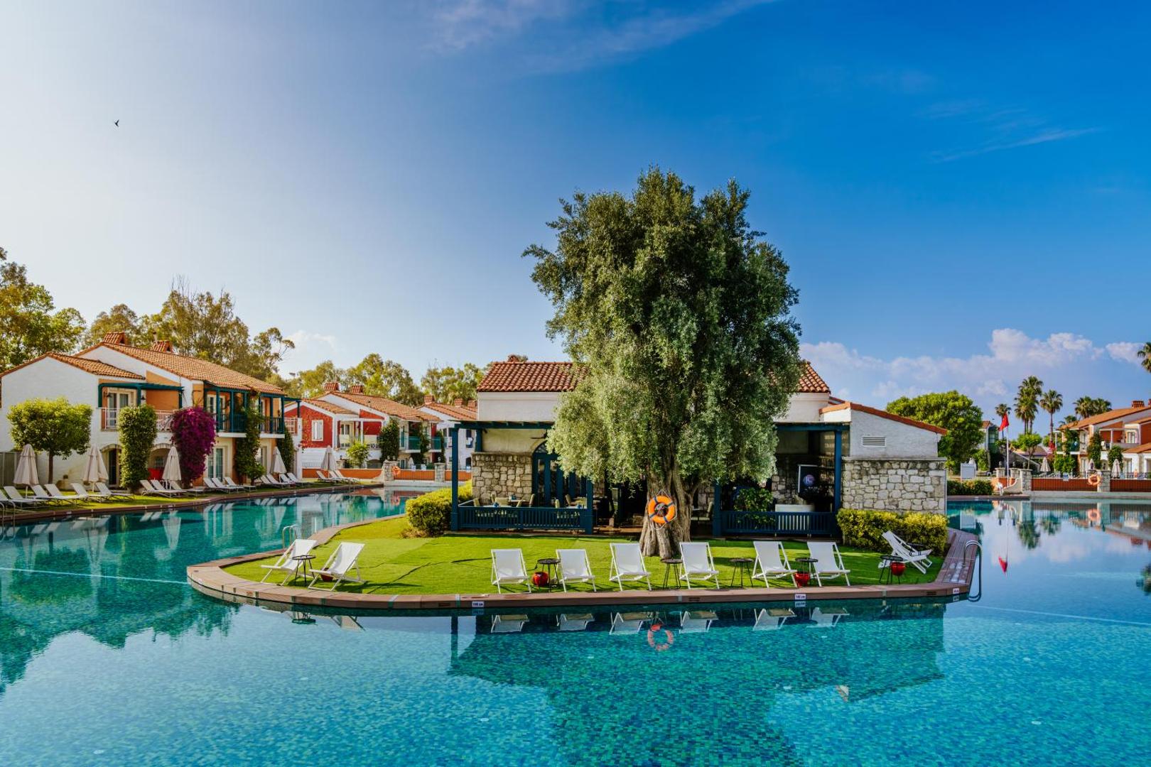 IC Hotels Santai Family Resort baseina zona ar atpūtas krēsliem zālājā un tradicionāla stila akmens ēkām fonā
