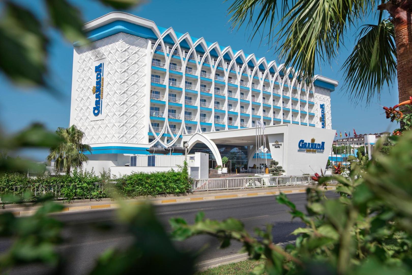 Granada Luxury Beach galvenā ieeja un modernā arhitektūra ar baltiem dekoratīviem elementiem un palmām piebraucamā ceļa malā