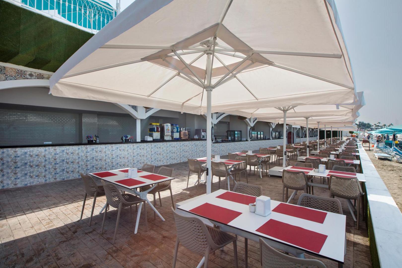 Granada Luxury Beach āra terases restorāns ar baltiem saulessargiem, galdiņiem un bufetes zonu netālu no pludmales smiltīm