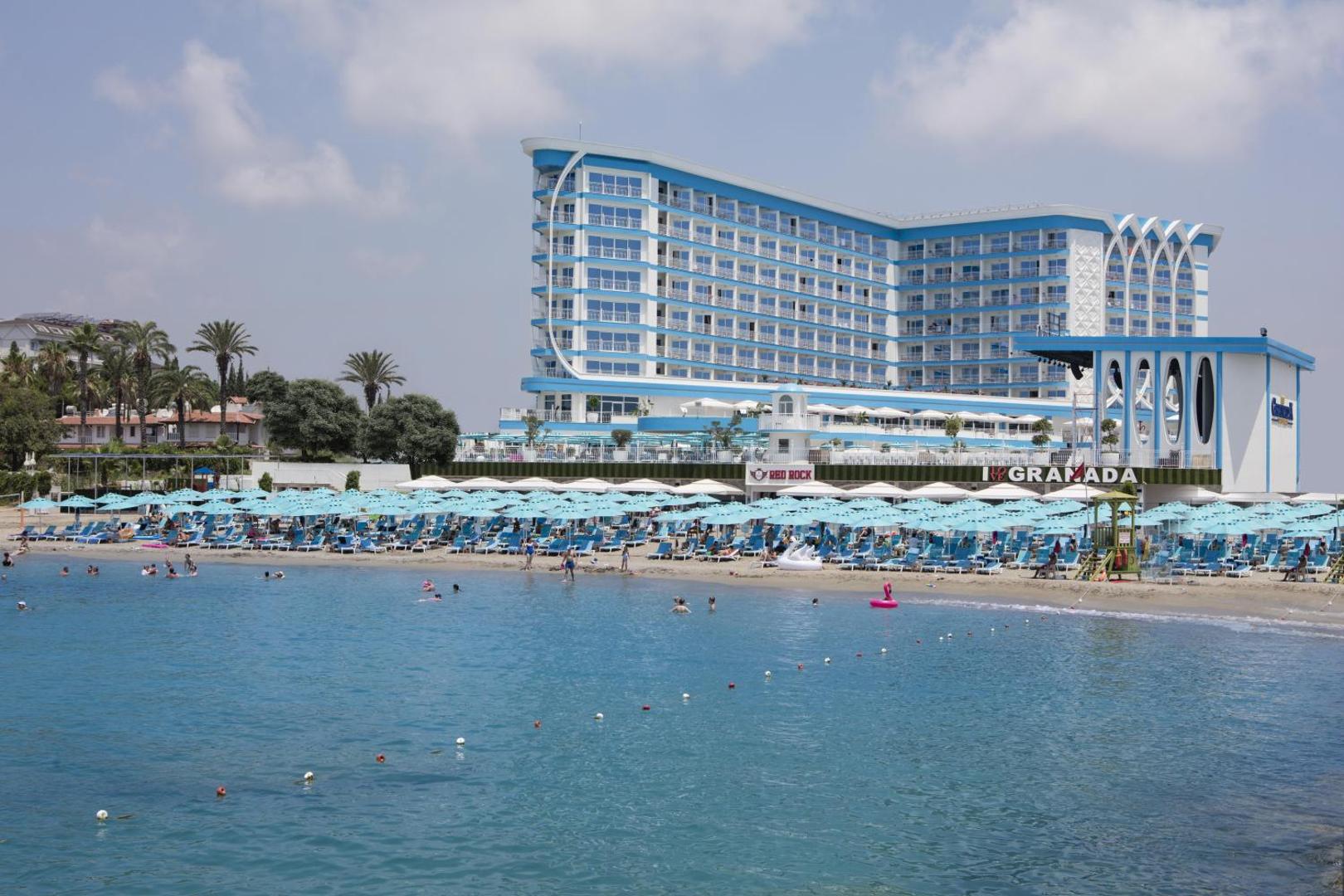 Granada Luxury Beach privātā pludmale ar gaiši ziliem saulessargiem un guļamkrēsliem pie dzidra jūras ūdens Alanjas reģionā, Turcijā