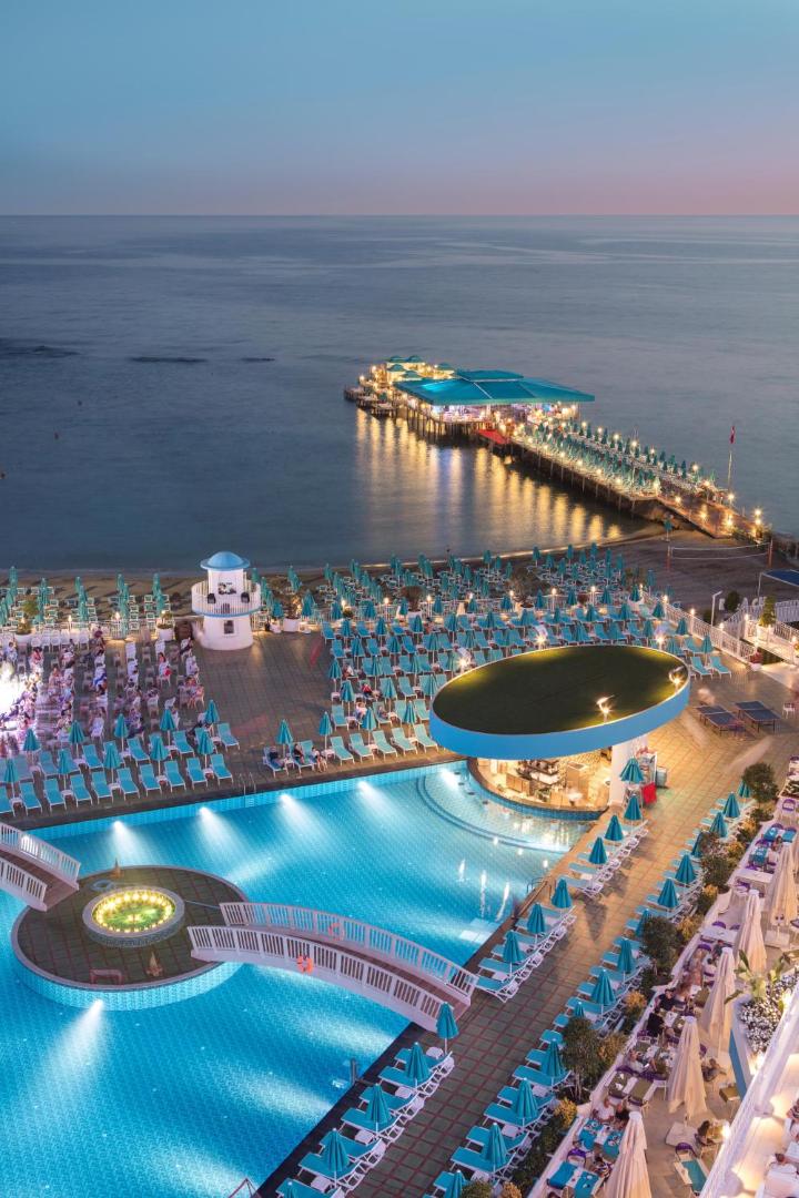 Granada Luxury Beach viesnīcas teritorijas skats no augšas vakarā — baseini, sauļošanās terases un mols jūrā