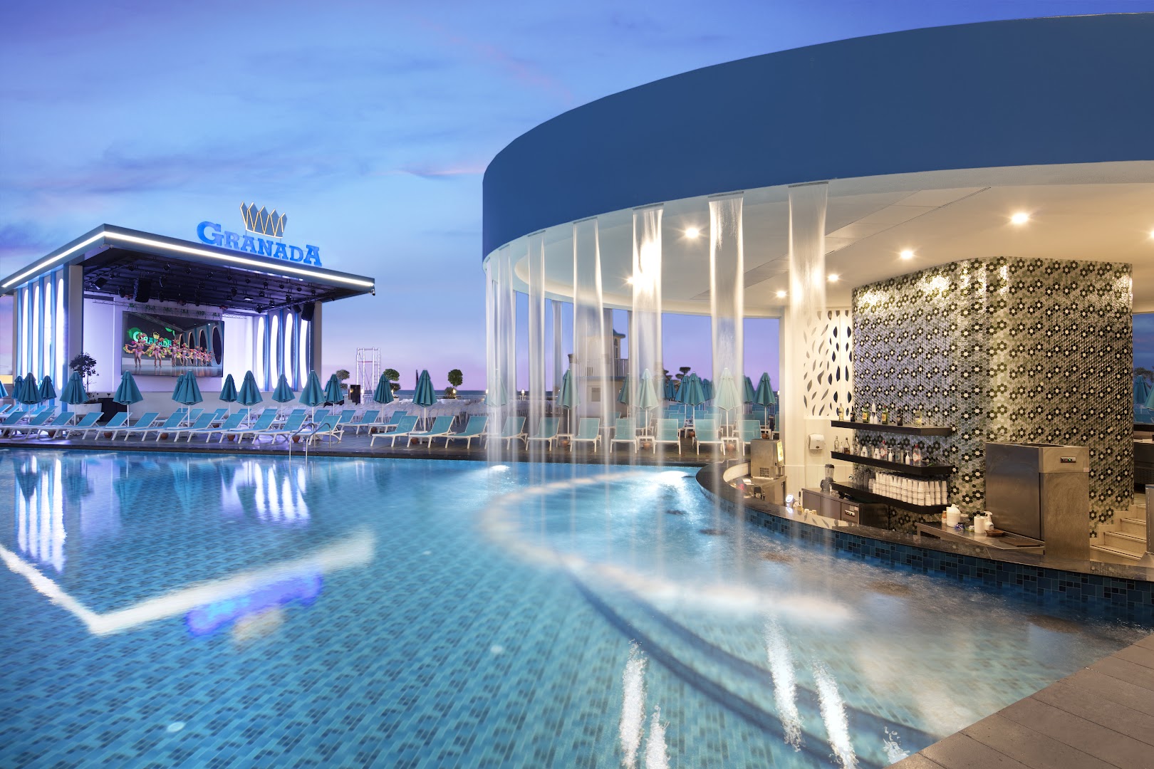 Granada Luxury Beach baseina bārs ar mākslīgo ūdenskritumu un skatu uz estrādi — moderna atpūtas zona pie ūdens
