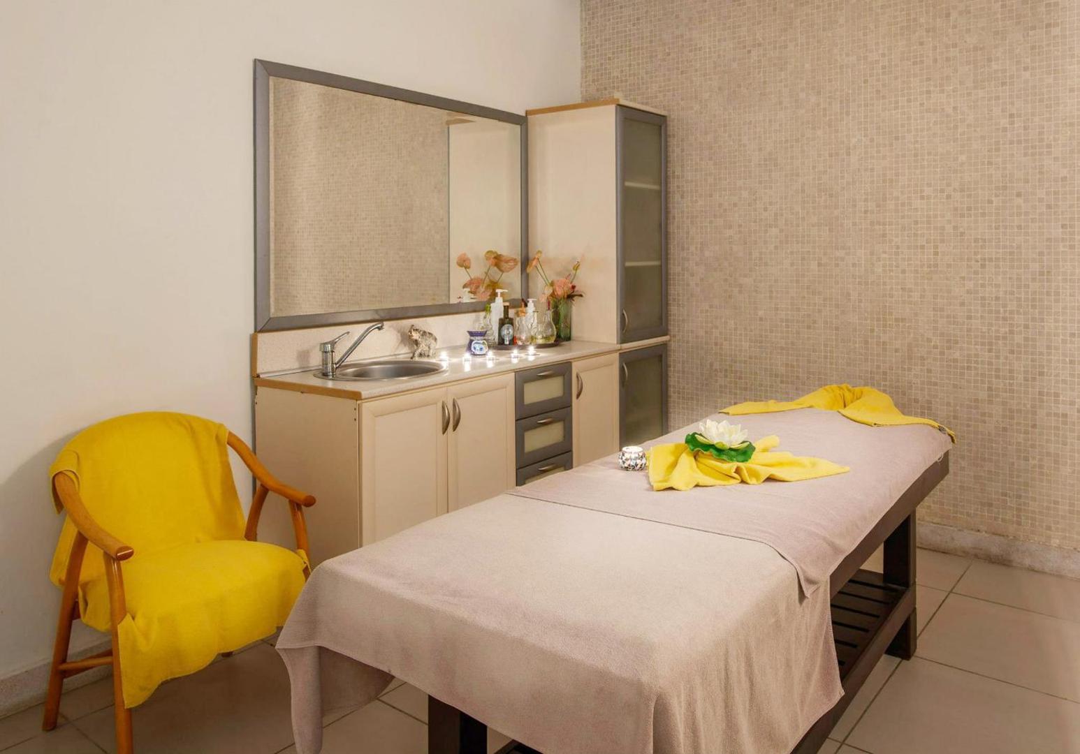 Golden Lotus spa centra masāžas telpa ar procedūru galdu, dzeltenu atpūtas krēslu un mierīgu apgaismojumu