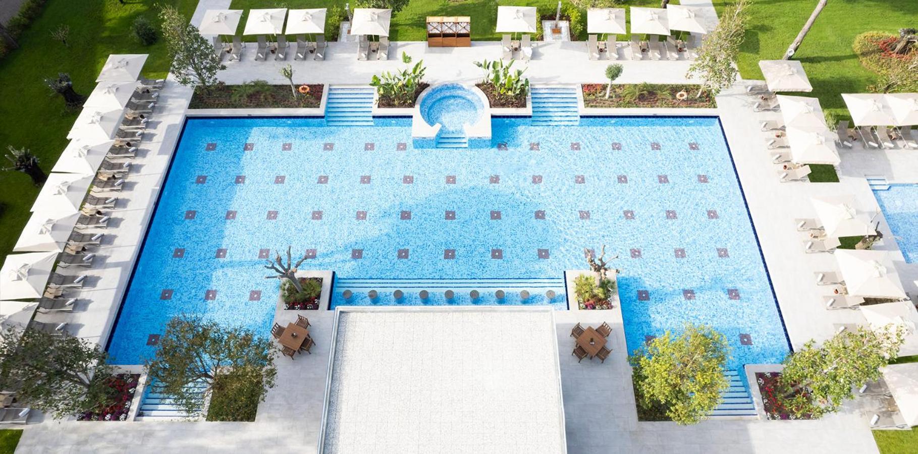Gloria Serenity Resort galvenais āra baseins ar simetrisku dizainu, atpūtas krēsliem, saulessargiem un koptu zālāju Belekas kūrortā